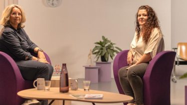 2 vrouwen zittend op paarse stoelen kijken naar de camera