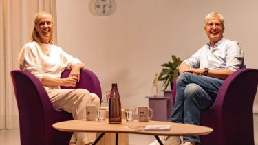 Man en vrouw lachen naar camera, zittend op paarse stoelen