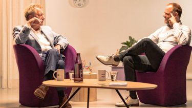 Twee mannen op paarse stoelen in gesprek met elkaar met een lage tafel ervoor