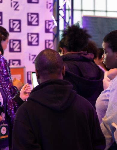 Meerdere mensen zijn met elkaar in gesprek bij een stand op een beursvloer van IZZ.