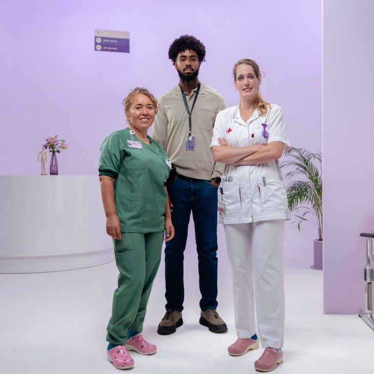 2 vrouwen en een man voor een paarse achtergrond in een ziekenhuisomgeving