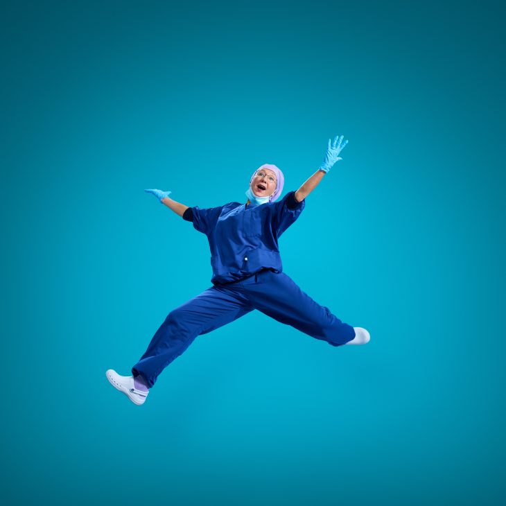 Een springende zorgmedewerker met handschoenen aan in een operatie pak.