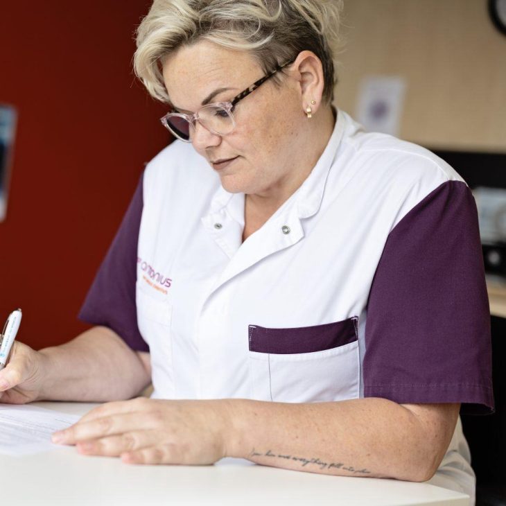 Vrouw in zorgoutfit tekent papieren