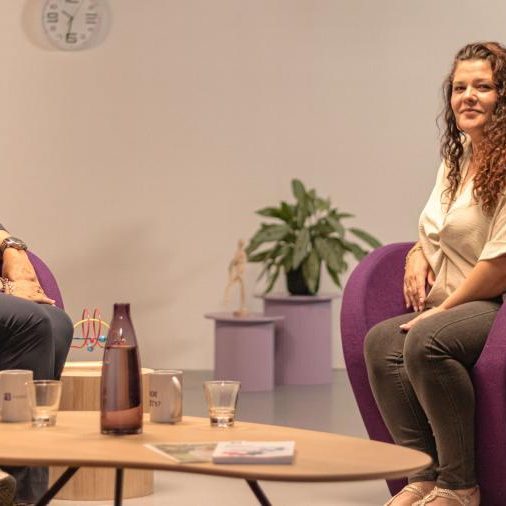 2 vrouwen zittend op paarse stoelen kijken naar de camera