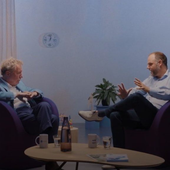 Twee mannen zittend in gesprek met elkaar op paarse stoelen