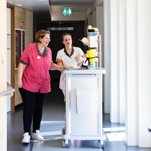 2 vrouwen lopen voor en naast kar in ziekenhuis