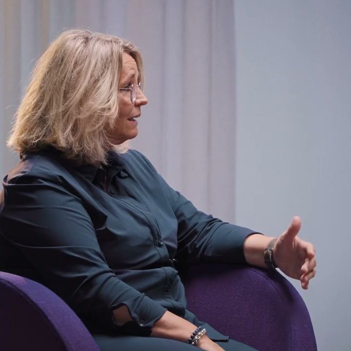 Vrouw in interview setting zit op paarse stoel