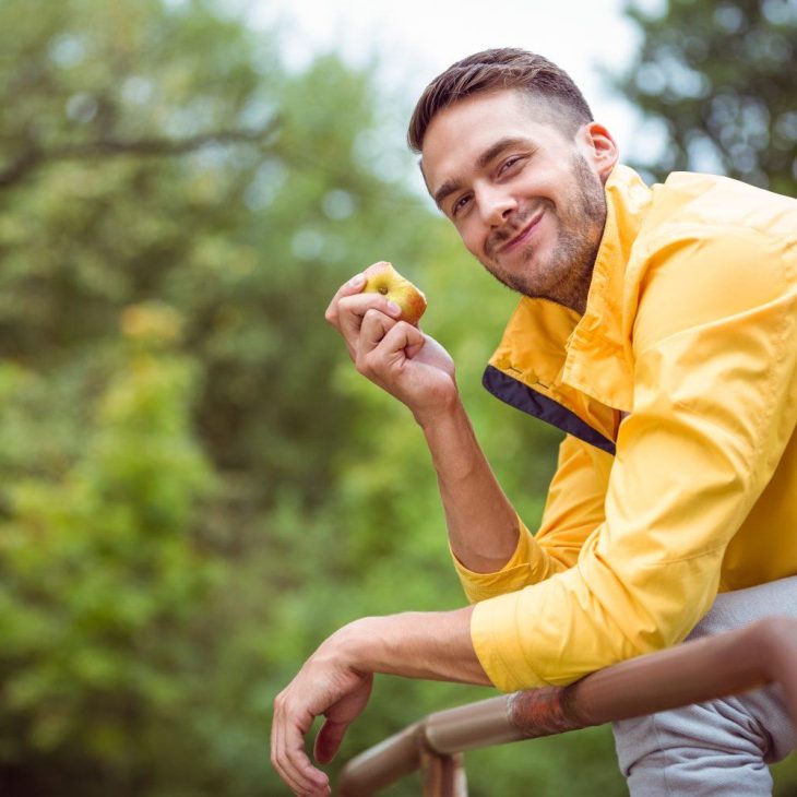 Man in gele jas eet appel en lacht naar camera