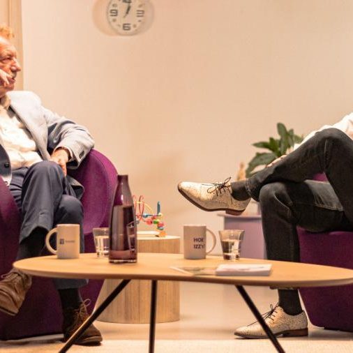 Twee mannen op paarse stoelen in gesprek met elkaar met een lage tafel ervoor